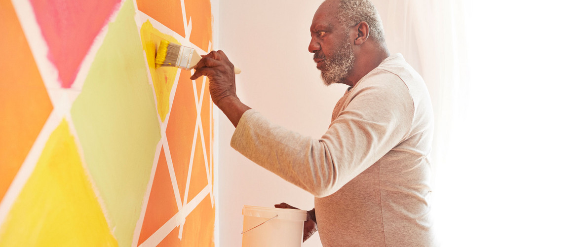 Mann streicht buntes Muster mit geometrischen Farben auf die Zimmerwand.