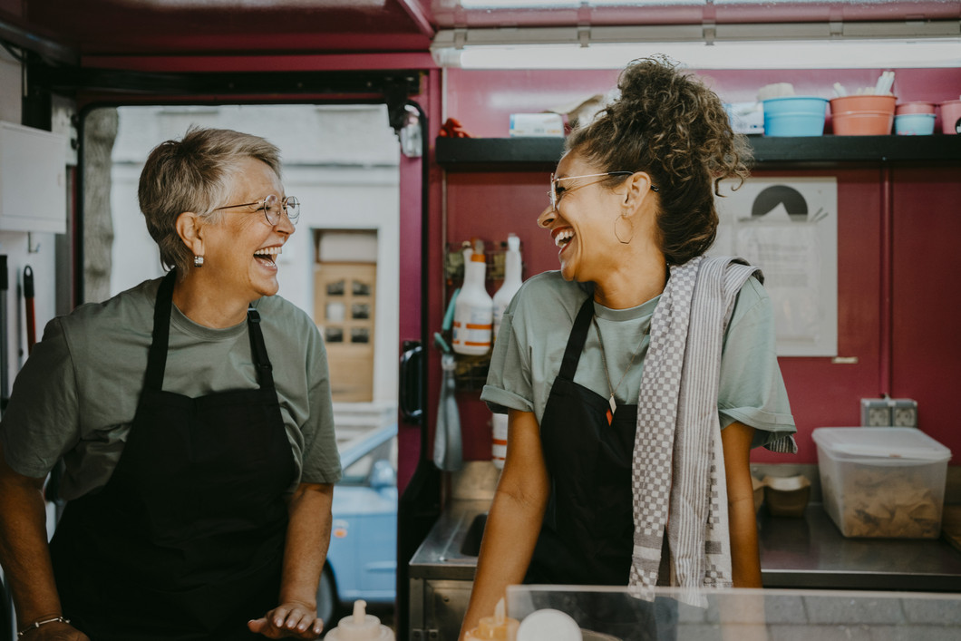 Zwei Frauen stehen in einem Foodtruck und lachen sich gegenseitig an