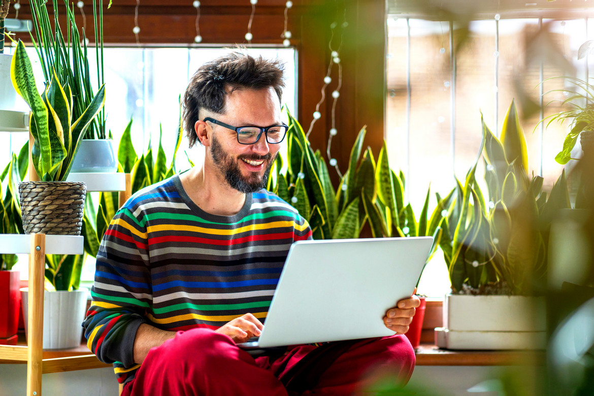 Mann mit schwarzen Haaren und Brille sitzt vor einem Laptop und lächelt. Er bucht gerade Kleinanzeigen PRO.