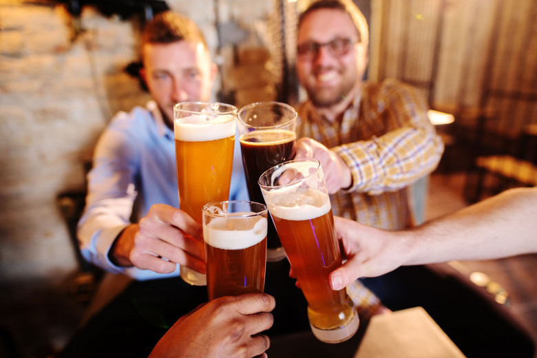 Vier Personen, von denen zwei zu sehen sind, stoßen mit Bier an