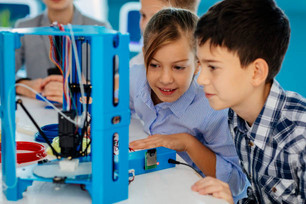 Junge und Mädchen beobachten gespannt einen 3D-Drucker