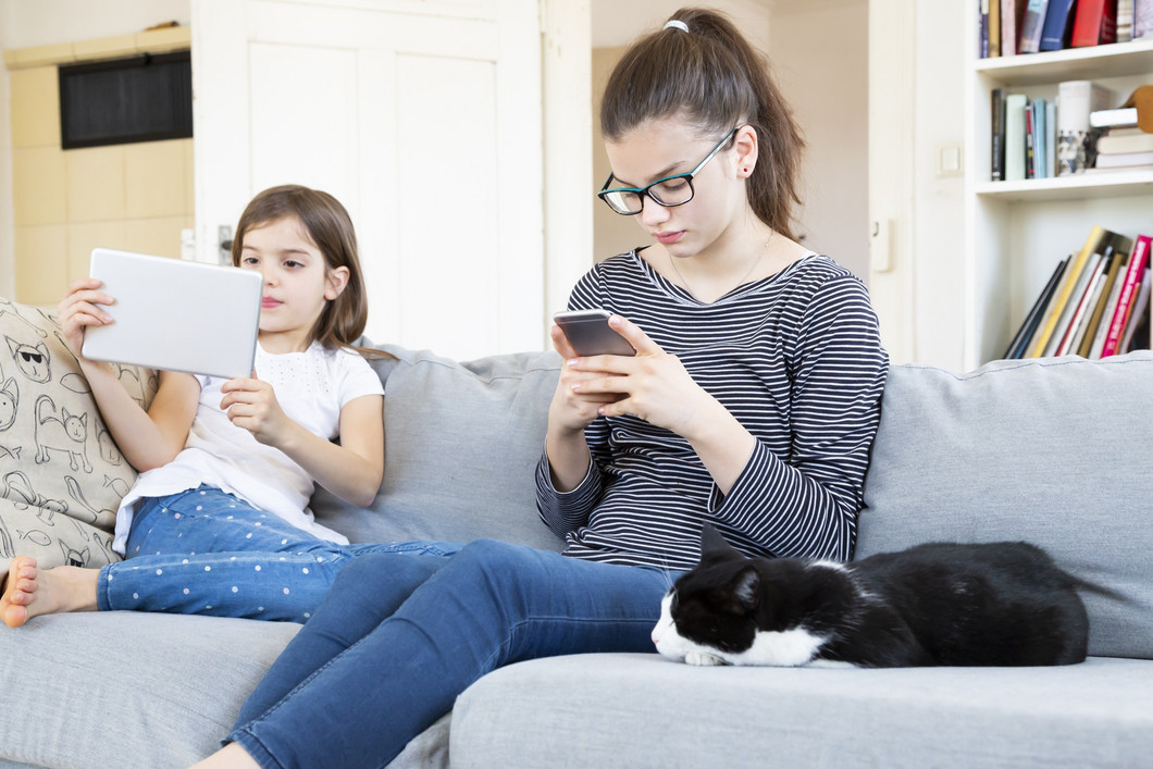 Geschwister sitzen auf Couch und nutzen Smarthone/Tablet