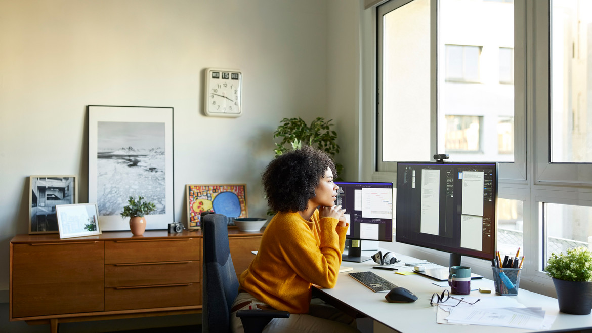 Eine Frau arbeitet konzentriert an zwei Monitoren in einem hellen Arbeitszimmer