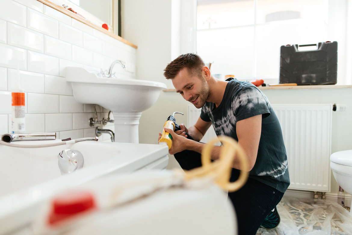 Ein Mann verarbeitet Silikon im Badezimmer für Schönheitsreparaturen