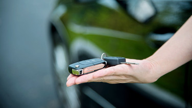 Schlüsselübergabe beim Autoverkauf - Hand überreicht Autoschlüssel.
