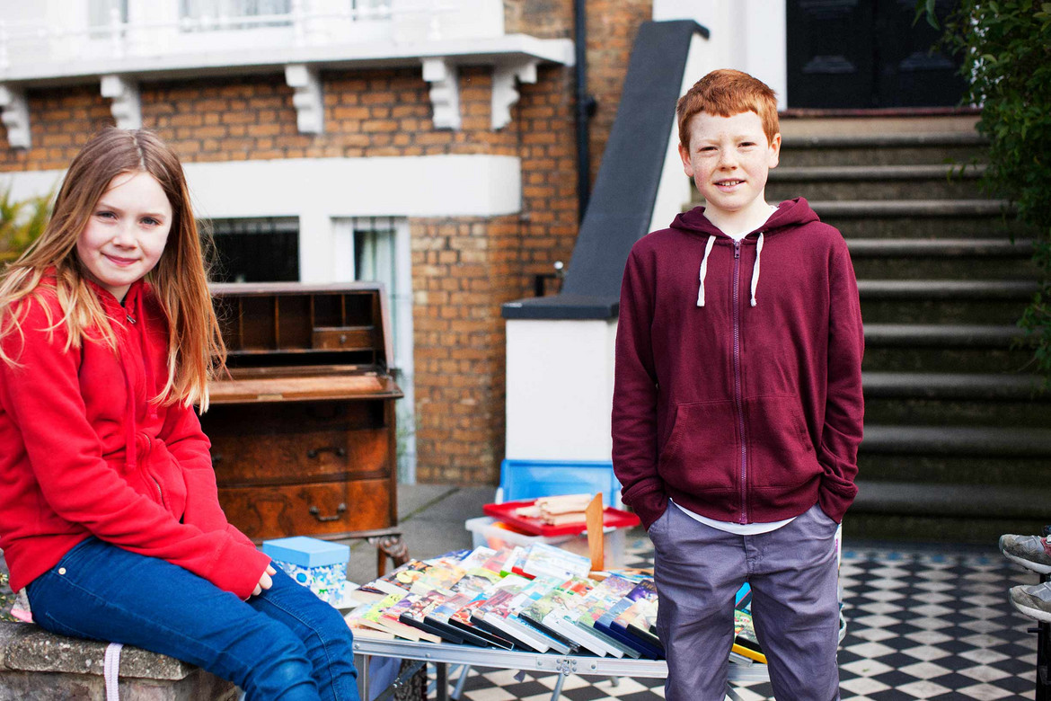 Junge und Mädchen stehen an kleinem Flohmarktstand mit Spielzeug vor ihrem Haus